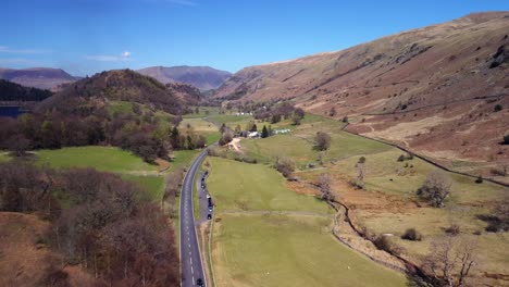 drone shot of lake district valley with a winding road, fields, and distant hills.