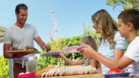 hombre sirviendo comida a la familia en el jardín de la casa