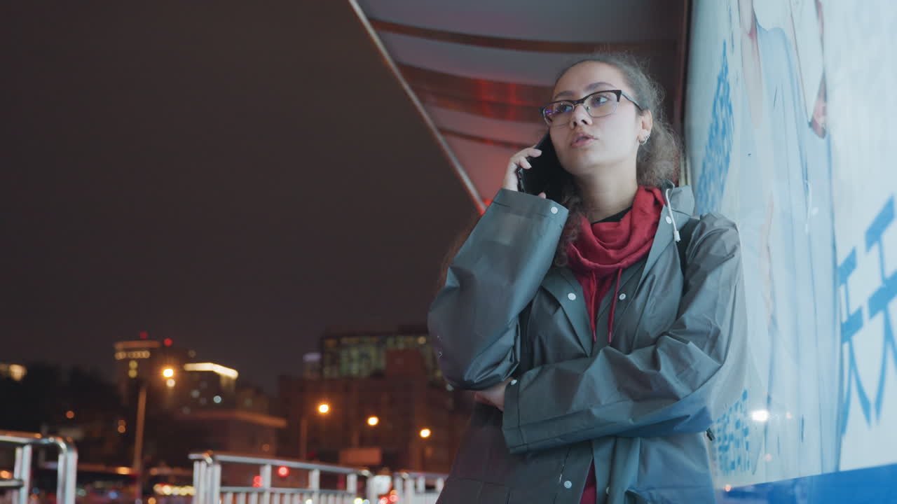 Giovane donna impegnata in una telefonata accanto a un vivace ambiente cittadino illuminato. Tranquilla scena serale con una donna in abito rosso immersa in una comunicazione pensierosa vicino a colorate opere d'arte urbana