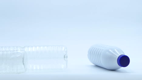 An-empty-recyclable-plastic-bottle-that-falls-on-top-of-two-others-that-are-standing-on-a-white-background