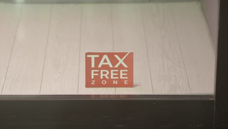 a red 'tax free zone' sign on a light-colored wooden floor, seen through a window