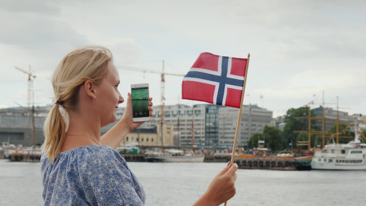 노르웨이 국기를 든 젊은 여성이 오슬로 시내를 배경으로 자신의 사진을 찍습니다.