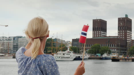 a young woman with a norwegian flag photographes herself against the background of the oslo city lin