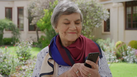 Porträt-Einer-älteren-Frau,-Die-Ihr-Smartphone-Nutzt,-Um-SMS-Zu-Schreiben-Und-Im-Online-Messaging-Zu-Surfen,-Lächelnd-Die-Mobile-Kommunikation-Im-Sonnigen-Garten-Im-Freien-Genießt