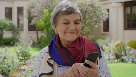 retrato de una mujer mayor usando un teléfono inteligente enviando mensajes de texto navegando por mensajes en línea sonriendo disfrutando de la comunicación móvil en un jardín soleado al aire libre