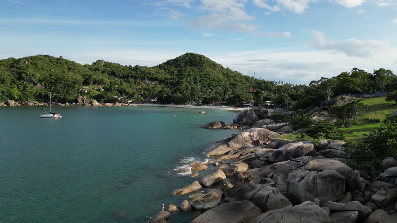 Static shot of a rocky shore near the mountains with still waters and a boat on the sea Koh Samui islands