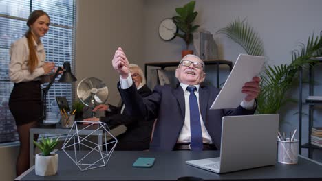 Cheerful-senior-company-boss-or-manager-laughing-and-being-surprised-with-colleagues-team-in-office