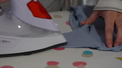 female hands ironing long sleeve of blue ribbed baby bodysuit at home. close up