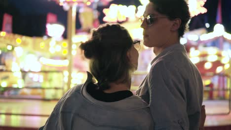 stylish hipster young couple are standing and looking for at amusement park. hugging. wearing blue similar shirts and sunglasses. footage from the backside
