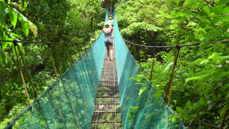 encantadora mujer asiática siguiendo al guía turístico mientras camina por un puente colgante en medio de un exuberante bosque verde en el nido, palawan, filipinas - plano medio