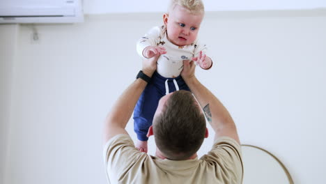 caucasian man holds his baby above the head. father plays with his son lifting him up.
