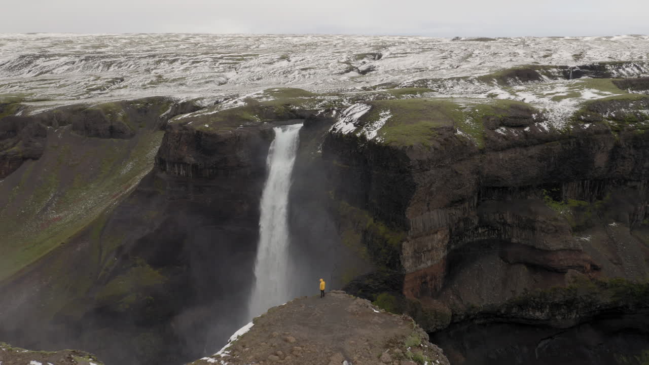 antena: un hombre con chaqueta amarilla, parado cerca del borde de un acantilado cerca de la cascada de haifoss en islandia