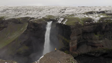 Aerial:-One-man-with-yellow-jacket,-standing-near-the-edge-of-a-cliff-near-Haifoss-waterfall-in-Iceland