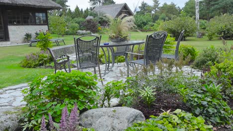 garden chair and table set in a beautiful garden during summer time while the weather is slightly cloudy and plants move in the wind