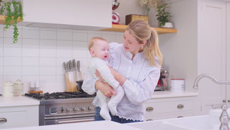 Madre-Amorosa-Llevando-A-Su-Hijo-Riendo-Alrededor-De-La-Cocina-En-Casa-Jugando-Juntos