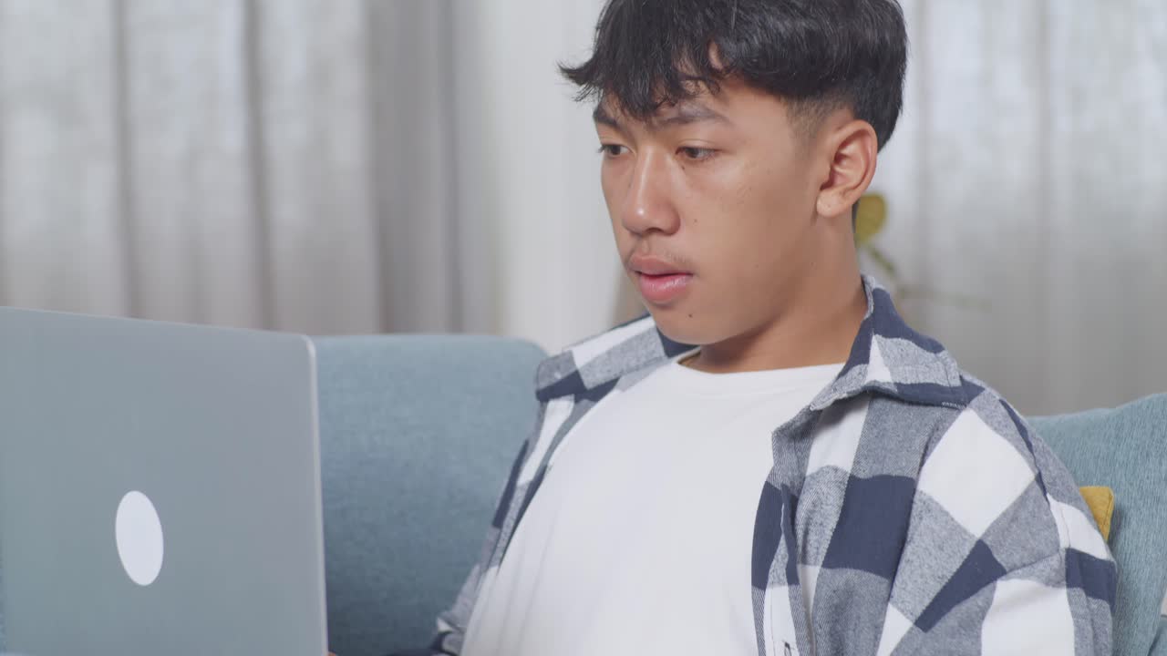 집 의 거실 의 소파 에 누워 있는 동안 노트북 에 타이핑 하는 간식 을 가진 아시아 청소년 소년 의 근접 사진