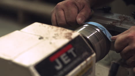 skilled laborer uses sandpaper on a piece of wood rotating on a factory lathe stabilized slider shot