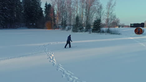 drone shot of a cross country skier approaching a sauna in latvia