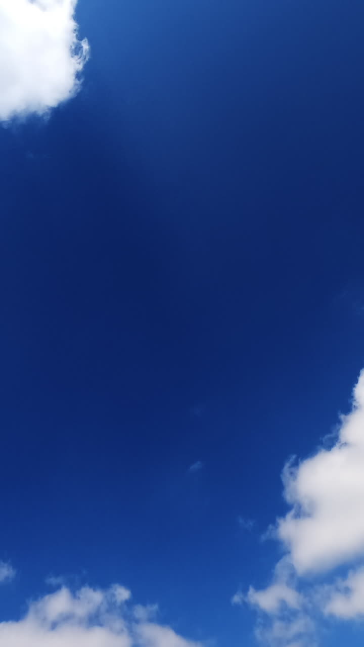 Light white clouds floating quickly in the bright blue skies. Fluffy clouds reflecting the rays of summer sun. Vertical video