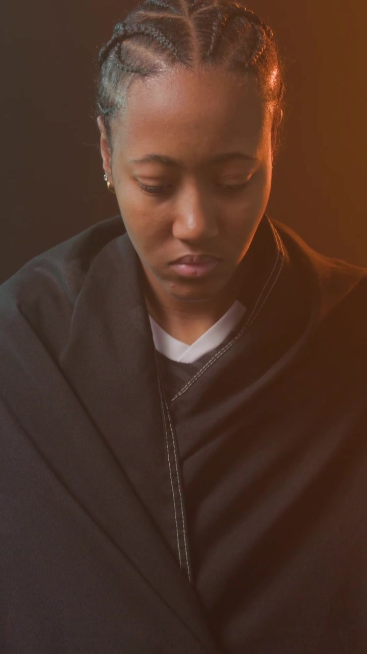 Vertical video: Camera tilting, woman in black hoodie adjusting jacket on grass, securing red drape