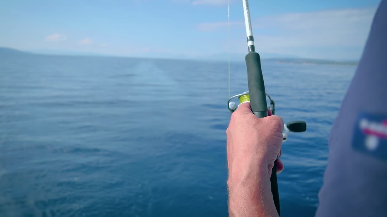 Mano di pescatore che tiene una canna da pesca mentre si trova su una barca a vela in mare - messa a fuoco selettiva.