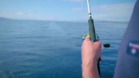 mano de pescador sosteniendo una caña de pescar mientras está de pie en un velero en el mar - enfoque selectivo