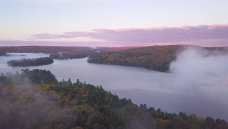 aerial sunrise wide shot flying through cloud fog to reveal misty lake with islands and pink clouds and fall forest colors in kawarthas ontario canada