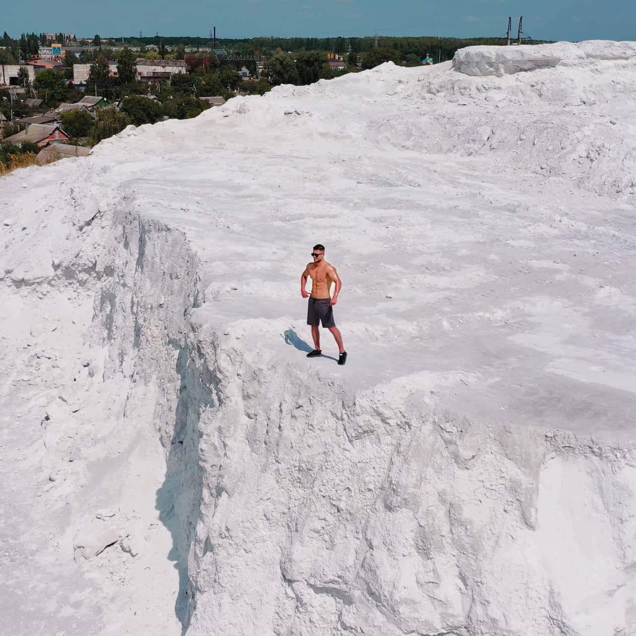 Muscular sportsman on a white hill. View from above on a strong guy who is showing his strength on the natural background. Bodybuilder on a rocky canyon. Aerial view.
