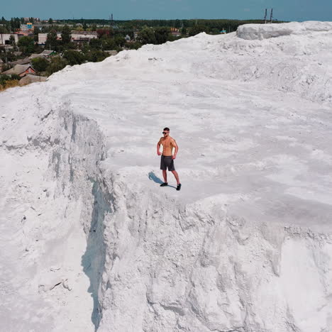 muscular sportsman on a white hill. view from above on a strong guy who is showing his strength on the natural background. bodybuilder on a rocky canyon. aerial view.