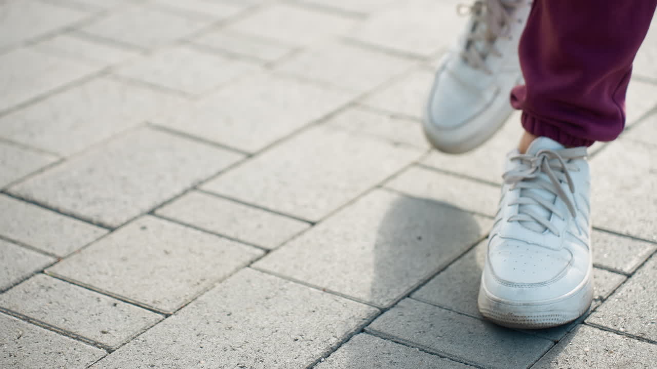 Leg view of runner walking on gray interlocking pavement under sunny sky casting long shadows capturing dynamic stride movement and sneaker detail in urban outdoor environment with morning light