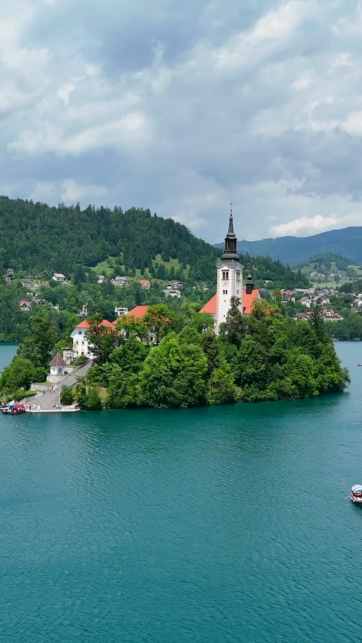 Isola di Bled con Chiesa, barche tradizionali Pletna sul lago, volo a bassa quota, verticale.