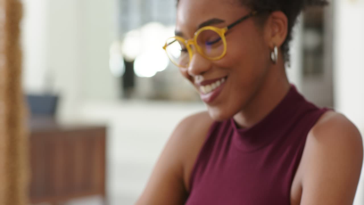 African woman reading notes, typing on laptop at desk, working with watch, looking up and smiling