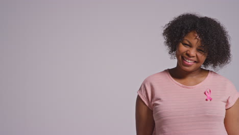 Retrato-De-Estudio-De-Una-Mujer-De-Mediana-Edad-Sonriente-Que-Viste-Ropa-Rosa-Y-Una-Cinta-De-Concientización-Sobre-El-Cáncer-De-Mama-Contra-Un-Fondo-Blanco