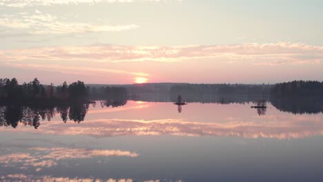 backing away aerial view over a perfectly mirrored lake in a forest during sunset in autumn