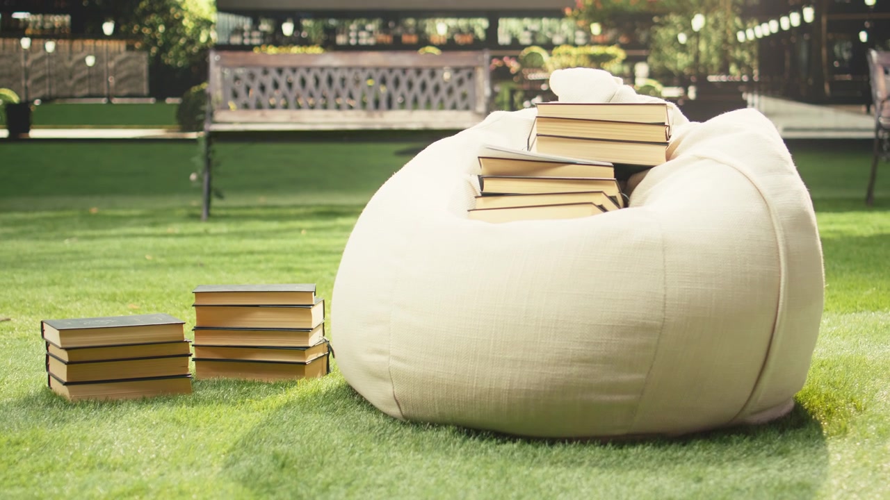 Pile di libri posizionate su un pouf su un prato soleggiato del campus