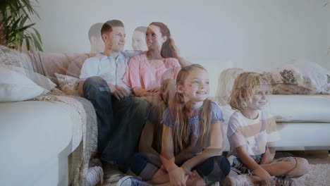 siblings sitting on the floor while watching tv with their parents behind them