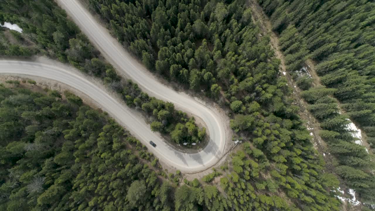 A car drives a hairpin turn in a forest in Canada's Rocky Mountains - Aerial footage