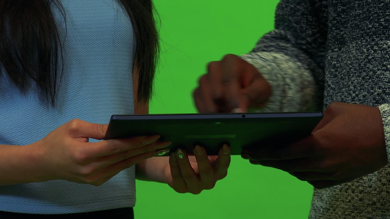 An Asian woman and a black man work on a tablet together - closeup - green screen studio