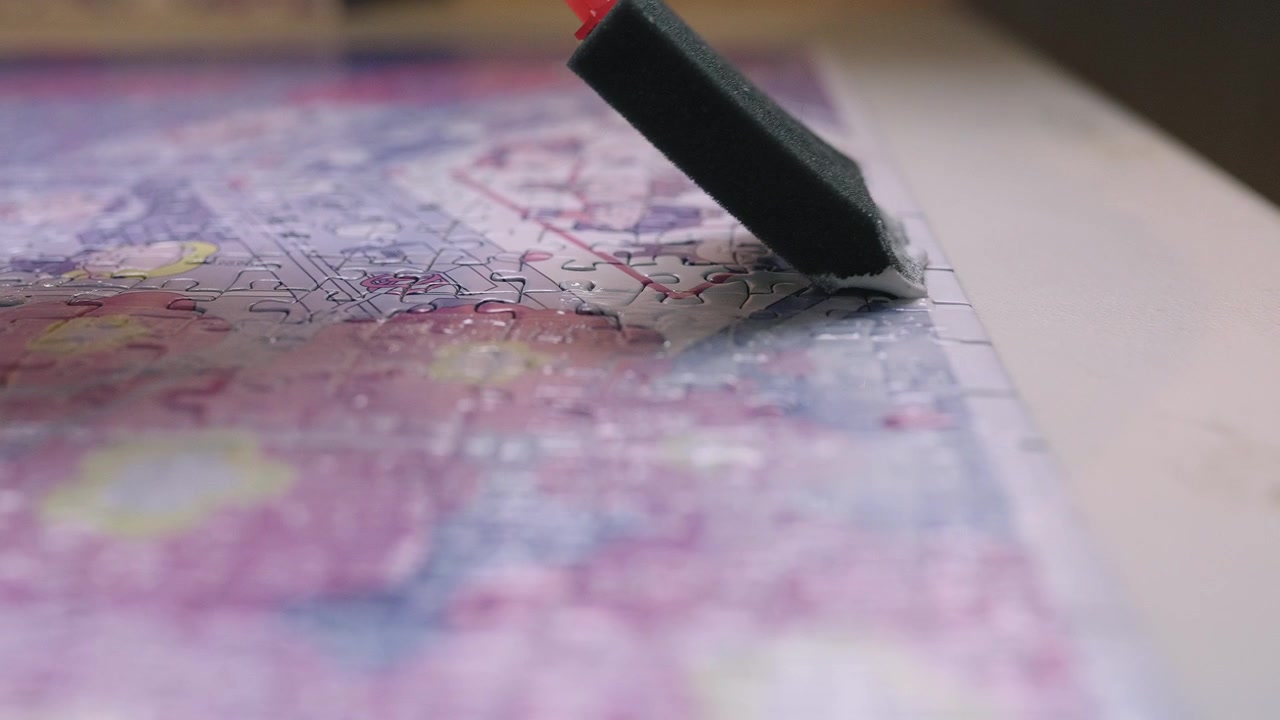Cola para quebra-cabeça Mod Podge sendo aplicada cuidadosamente em um quebra-cabeça montado