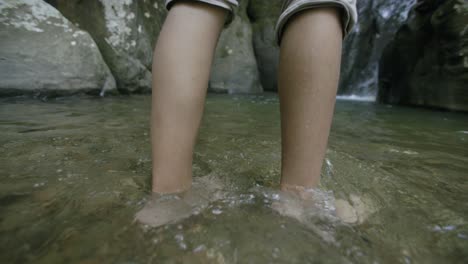 slow motion footage following the feet of a young african american man as they go through the water of a stream