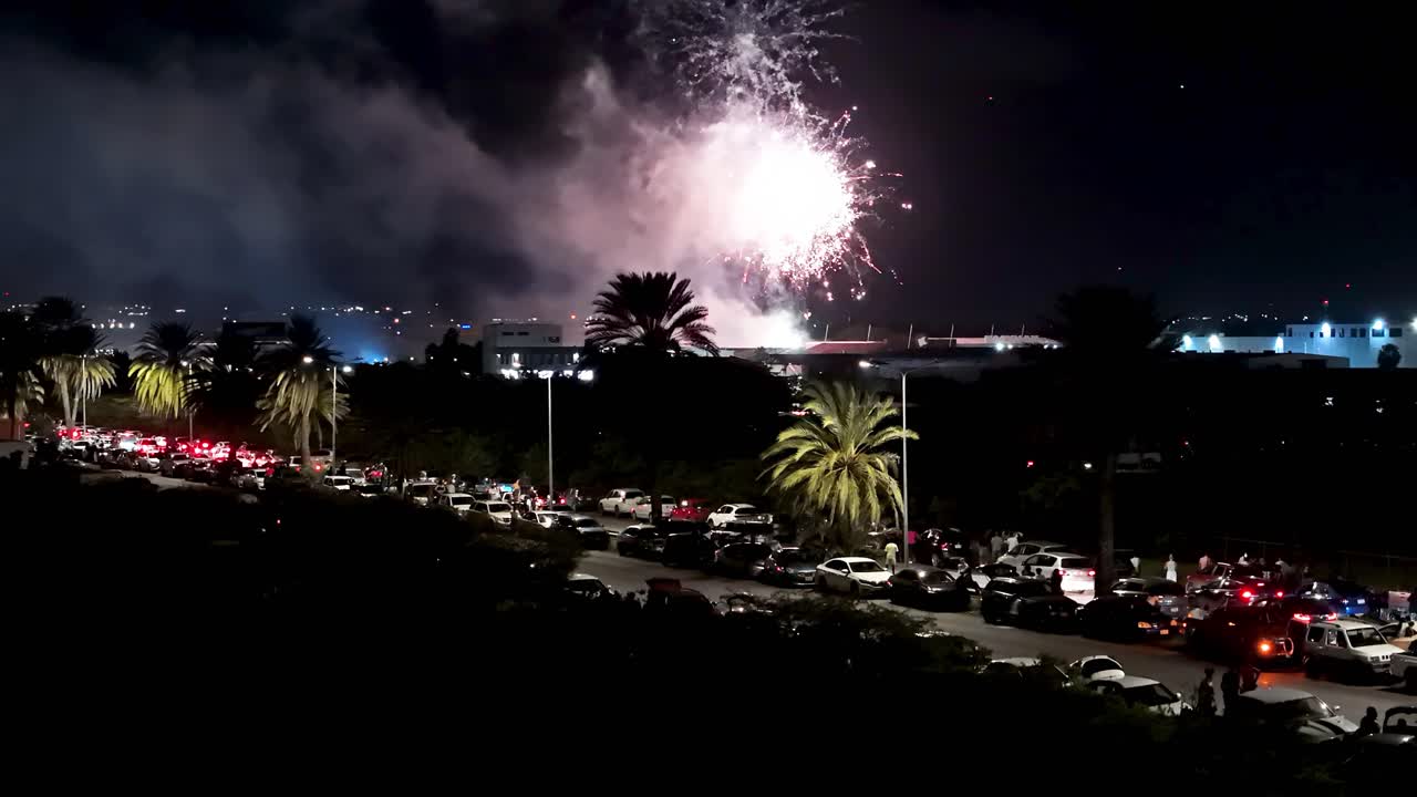 los fuegos artificiales aéreos se lanzan alto en el cielo por encima de las palmeras paseo tropical como los coches de la línea de la carretera para ver la columna de humo y la luz brillante