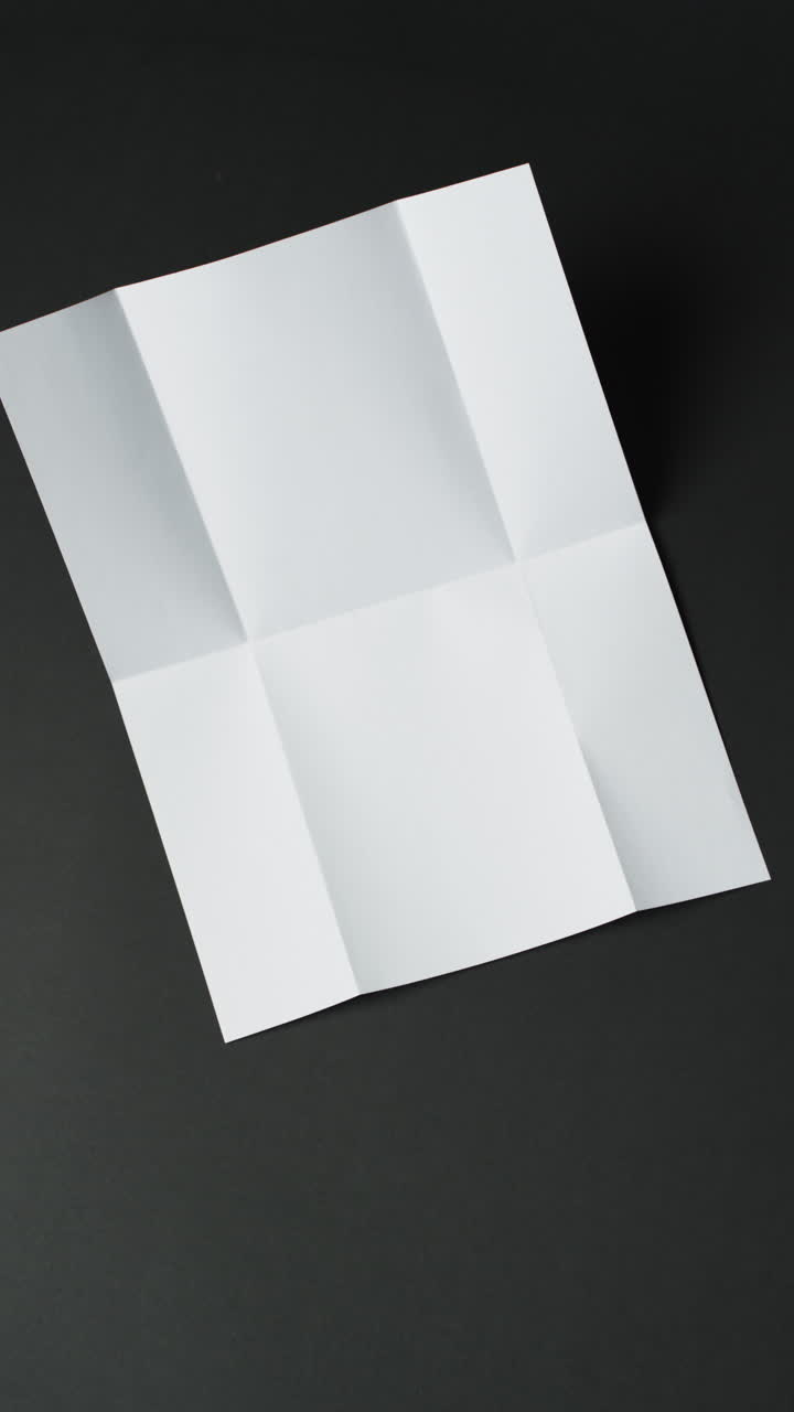 Vertical video of piece of white paper with creases on black background