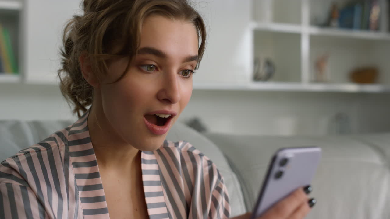 Surprised woman using smartphone reading messages in pajamas at home closeup.