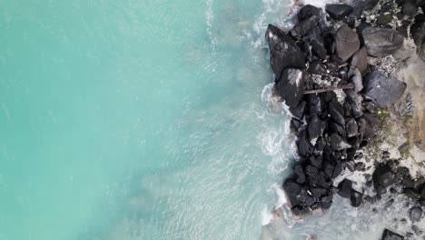 Relajante-Toma-Aérea-Amplia-De-Agua-Rompiendo-En-Las-Rocas-En-La-Orilla-De-La-Playa-Arena-Cielo-Azul-Nubes-Blancas-Agua-Turquesa-Relajación-Turismo-De-Vacaciones