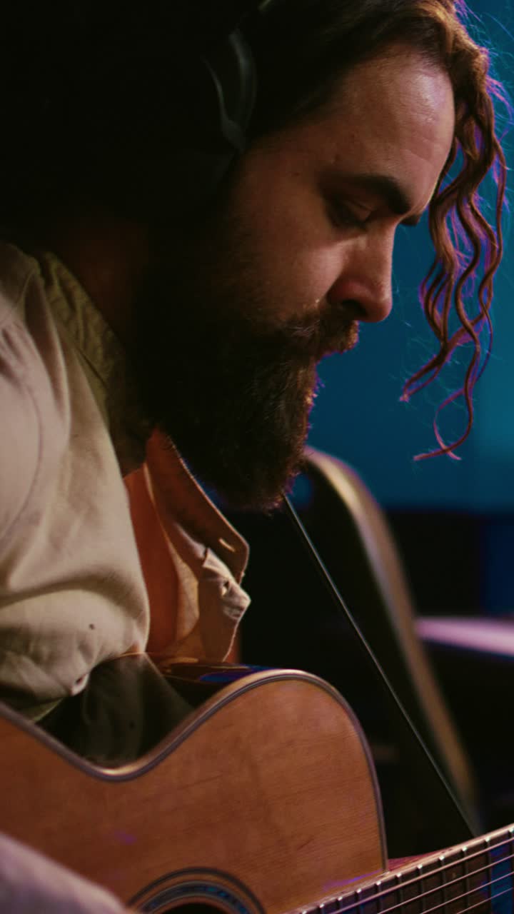Hombre con auriculares tocando la guitarra acústica en un estudio de grabación
