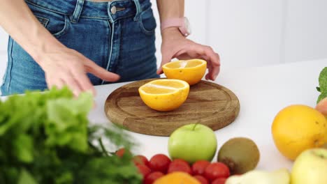 female hands cut with a knife a ripe yellow orange on a wooden kitchen board