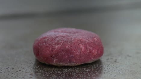 close-up of a raw burger patty on a restaurant grill as black pepper is ground on top