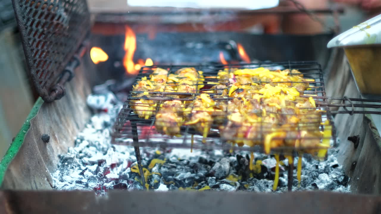 Lathering curried lamb skewers being grilled on wood fire with sauce, close-up