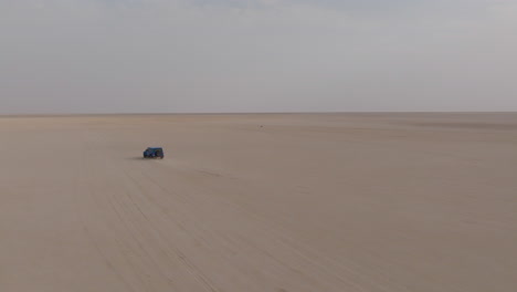 lonely 4x4 car drives across empty desert to bar al hikman, oman, aerial wide view