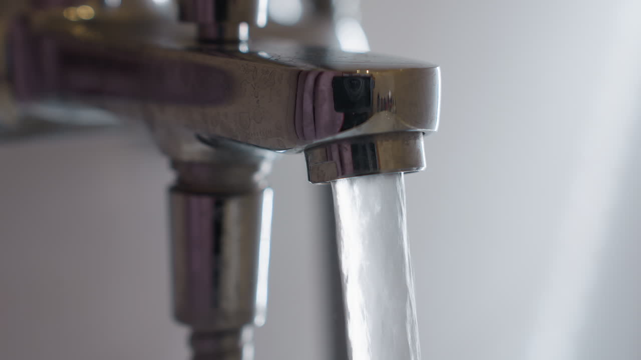 Close up of water rushing from shiny chrome tap in bathroom, stream flowing smoothly into sink, capturing detail of plumbing, water pressure, hygiene and daily household routine
